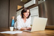 © Halfpoint - Mature woman working from homeoffice. Woman paying bills online, lying on floor.
