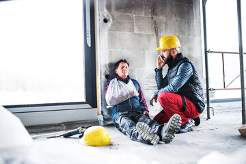 Colleague calling ambulance and giving first aid to injured worker, in pain after accident at construction site Concept of occupational safety and health in workplace.