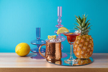 Wall Mural - Summer creative concept with drink, lemon, pineapple and  mirrored tray on wooden table over blue background