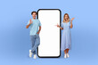 © Prostock-studio - European couple smiles are infectious as they stand side by side, presenting a large smartphone with a pristine, empty screen, ready to capture the imagination.