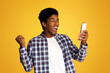 © Prostock-studio - Winner Concept. African Guy Using Smartphone over Yellow Studio Background