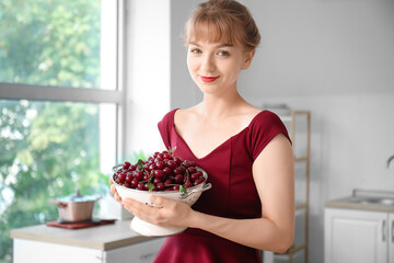 Poster - Happy beautiful young woman with colander full of ripe cherries in kitchen