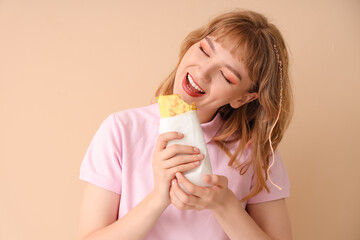 Canvas Print - Young woman eating tasty sandwich wrap on beige background