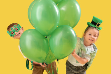 Wall Mural - Cute kids with festive green outfits and balloons on yellow background. St. Patrick's Day celebration