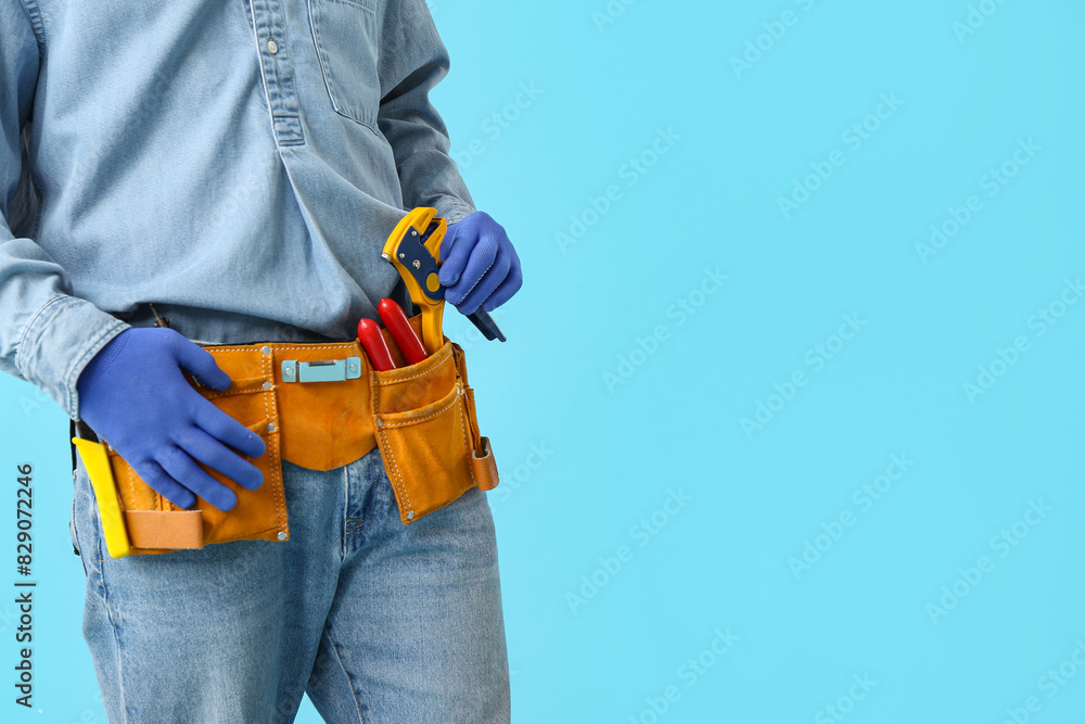 Male electrician with tool belt on blue background