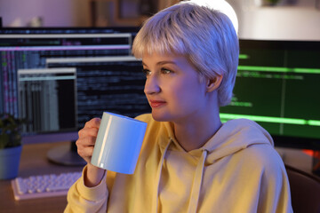 Wall Mural - Young female programmer drinking coffee in office at night, closeup