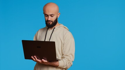 Middle eastern man works with cyber security on laptop, trying to do some software programming and report bugs. Young adult operating as a system developer in studio. Camera 2. Handheld shot.