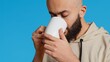 © DC Studio - Middle eastern guy drinking cup of coffee in studio, enjoying fresh aroma of caffeine refreshment. Arab person standing over blue background, taking a sip from mug. Camera 2. Handheld shot.