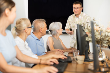 Wall Mural - Inspiring instructor leading computer session for older adults. Concept of digital education for seniors..