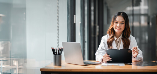 Wall Mural - A woman is sitting at a desk with a laptop and a tablet. She is smiling and she is happy