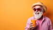 © worawut - Vibrant and colorful summer concept with a happy old man in a hat and sunglasses sipping an orange juice or cocktail on a pastel background A trendy hipster senior person enjoying