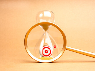 Short-term business goals encompass work that helps an organization reach its mid-term goals concept. 3d Target dart icon in hourglass focused in magnifying glass lens isolated on bright background.