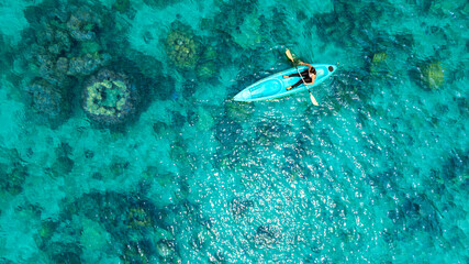 Wall Mural - Aerial view of a woman and a young man kayaking on clear blue waters at Andaman Island. She does water sports activities.	