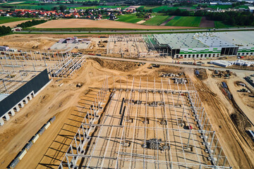 Aerial view of construction site with warehouse building under construction for storage. Assembling industrial building with steel frame structure and roof truss. Infrastructure for logistics