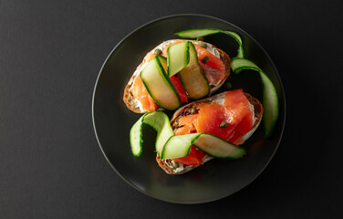 Wall Mural - Sandwiches with smoked trout, cream cheese, fresh cucumber, and capers on a black plate.