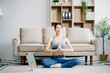 © Nuttapong punna - Asian Woman Doing Yoga and Watching Online Tutorials on Laptop, Training in Living Room at home