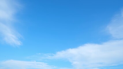Wall Mural - A clear blue sky with a few scattered, wispy white clouds. The sky transitions smoothly from a deeper blue at the top to a lighter blue near the horizon, creating a serene and expansive atmosphere.
