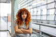 © Westend61 - Upset redhead young woman with arms crossed looking out through window