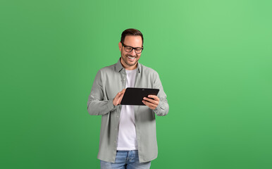 Wall Mural - smiling young businessman in eyeglasses reading e-mails over digital tablet on green background