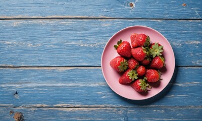 Red ripe strawberries on a pink plate, blue wood background