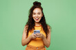 © ViDi Studio - Young surprised shocked woman of African American ethnicity wearing yellow tank shirt top hold in hand use mobile cell phone isolated on plain pastel light green background studio. Lifestyle concept.