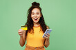 © ViDi Studio - Young surprised woman wear yellow tank shirt top using mobile cell phone hold credit bank card doing online shopping order delivery booking tour isolated on plain green background. Lifestyle concept.