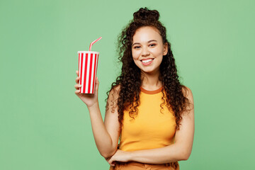 Wall Mural - Young woman of African American ethnicity wear yellow tank shirt top hold in hand cup of soda pop cola fizzy water isolated on plain pastel light green background studio portrait. Lifestyle concept.