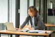 © Thitisak - Asian business woman working on computer looking at documents at office