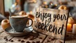 © Chananporn - A cup of coffee with a 'Enjoy your weekend' sign on a rustic wooden table with scattered coffee beans.