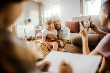 Wall Mural - Happy family playing together at home with child being photographed