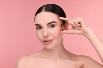 Wall Mural - Beautiful young woman holding skincare ampoule on pink background