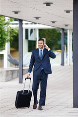 Canvas Print - Phone call, walking or businessman with luggage or suitcase in conversation, chat or deal communication. Outdoor, travel and happy financial advisor networking for investment, negotiation or news