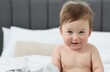 © New Africa - Happy baby boy with blanket and rattle sitting on bed at home