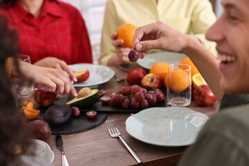 Wall Mural - Vegetarian food. Friends eating fresh fruits at wooden table indoors, closeup
