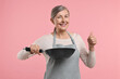 © New Africa - Happy housewife with frying pan showing thumbs up on pink background