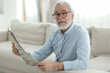 © New Africa - Portrait of grandpa with stylish glasses reading newspaper on sofa indoors