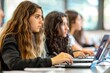 © Ilia Nesolenyi - Several young women are seated at a table, focused on their laptops. They appear to be engaged in a learning activity