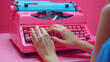 © AS Photo Family - A close-up of hands typing on a vibrant pink vintage typewriter against a pink background
