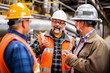 © apratim - A group of factory workers and engineers discussing a project in an industrial environment, wearing safety gear and hard hats.