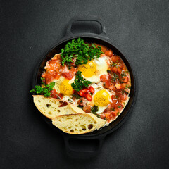 Wall Mural - Tasty Breakfast Shakshuka in an Iron Pan. Fried eggs with tomatoes. On a black stone background.
