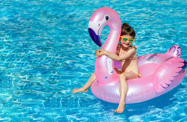 A little girl 5-6 years old, sitting in a pink flamingo inflatable pool float, highlighting summer activities and children's pool safety equipment