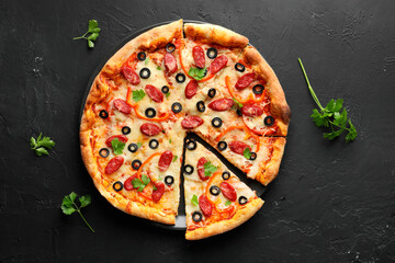 Tasty pizza with dry smoked sausages, olives, pepper and parsley on black table, top view