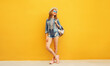 © rohappy - Beautiful young woman full length standing in summer hat with backpack, denim clothing on yellow