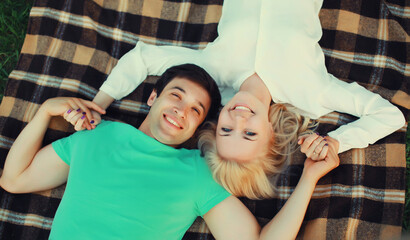 Poster - Portrait of beautiful happy smiling young couple in love lying together on a blanket, summer park