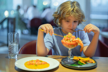 Wall Mural - Little boy eating seafood in restaurant. Kid eat Food fish gourmet seafood shrimp in restaurant. Adorable little boy at restaurant having breakfast.