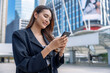 © Basicdog - Businesswoman uses phone while standing on the street in big city.