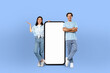 © Prostock-studio - A man and woman standing next to a blank screen, posing for a picture. The man is wearing a dark suit while the woman is dressed in a white blouse and black pants.
