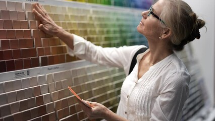 Wall Mural - Closeup of smiling mature woman comparing color swatches at a paint display shopping for home redecorating renovation project, in a hardware store.