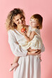 © LIGHTFIELD STUDIOS - Mother and daughter holding an apple on a pink background.