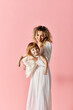© LIGHTFIELD STUDIOS - A mother with curly hair holds her baby on a pink background.